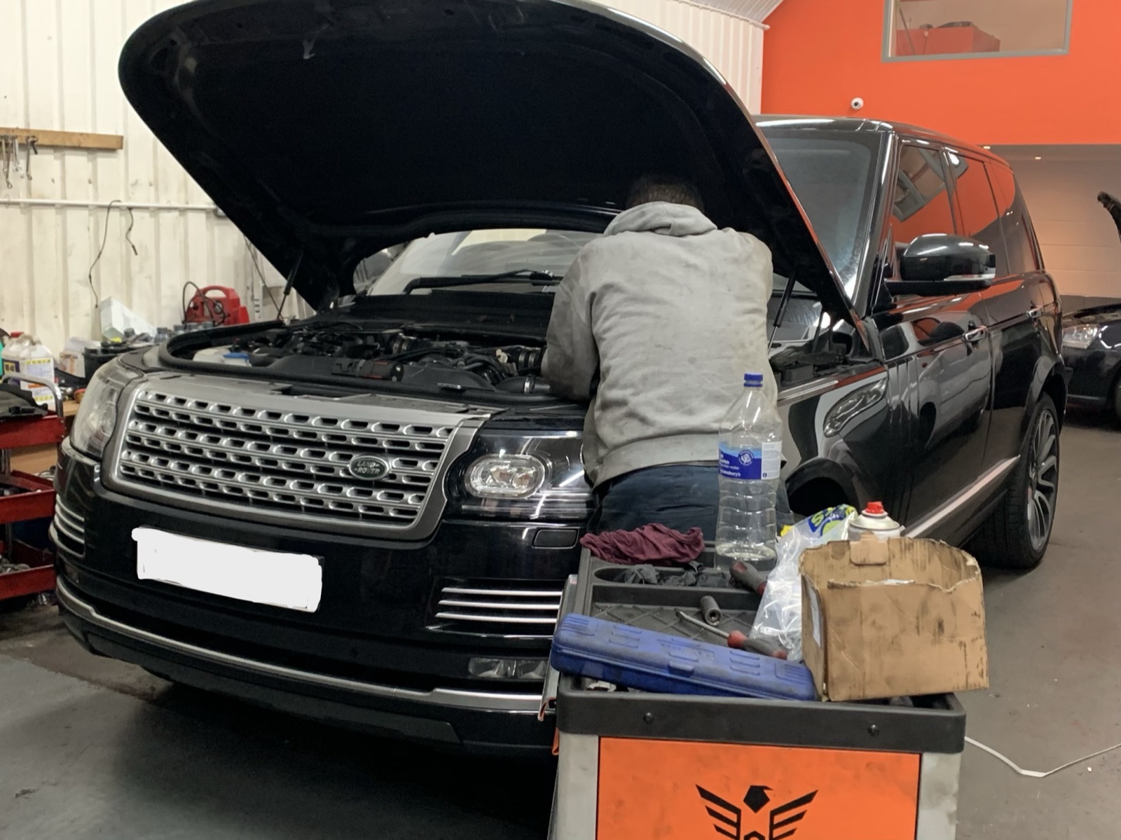 A mechanic working under the bonnet of a black Range Rover at Witan Motors during an engine diagnosis.