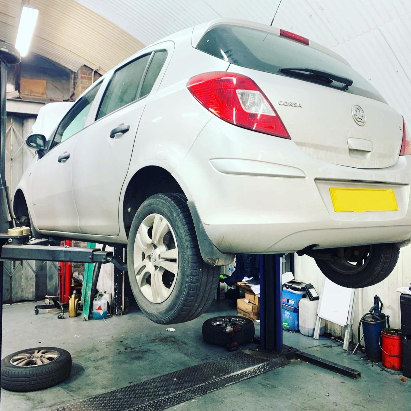 A white Vauxhall Corsa raised on the two-post ramp at Witan Motors with a wheel removed for brake work.